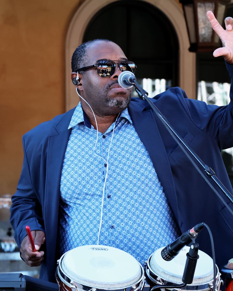 Niobel Cintra in a blue suit and sunglasses, one hand raised, singing.